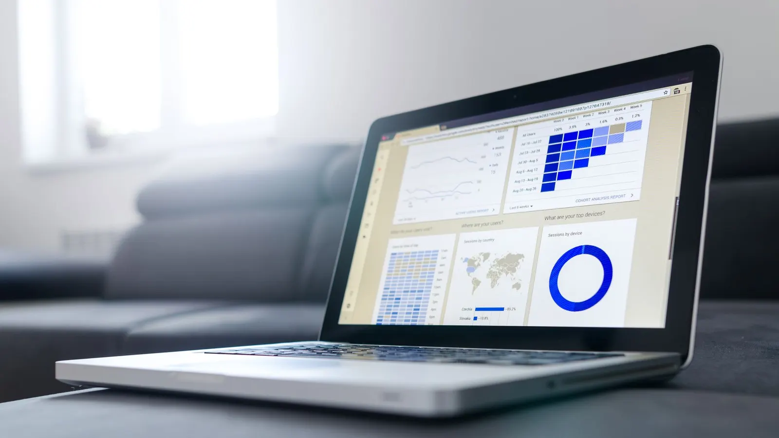 A laptop on a low table showing a web analytics dashboard, with visitor charts and a world map