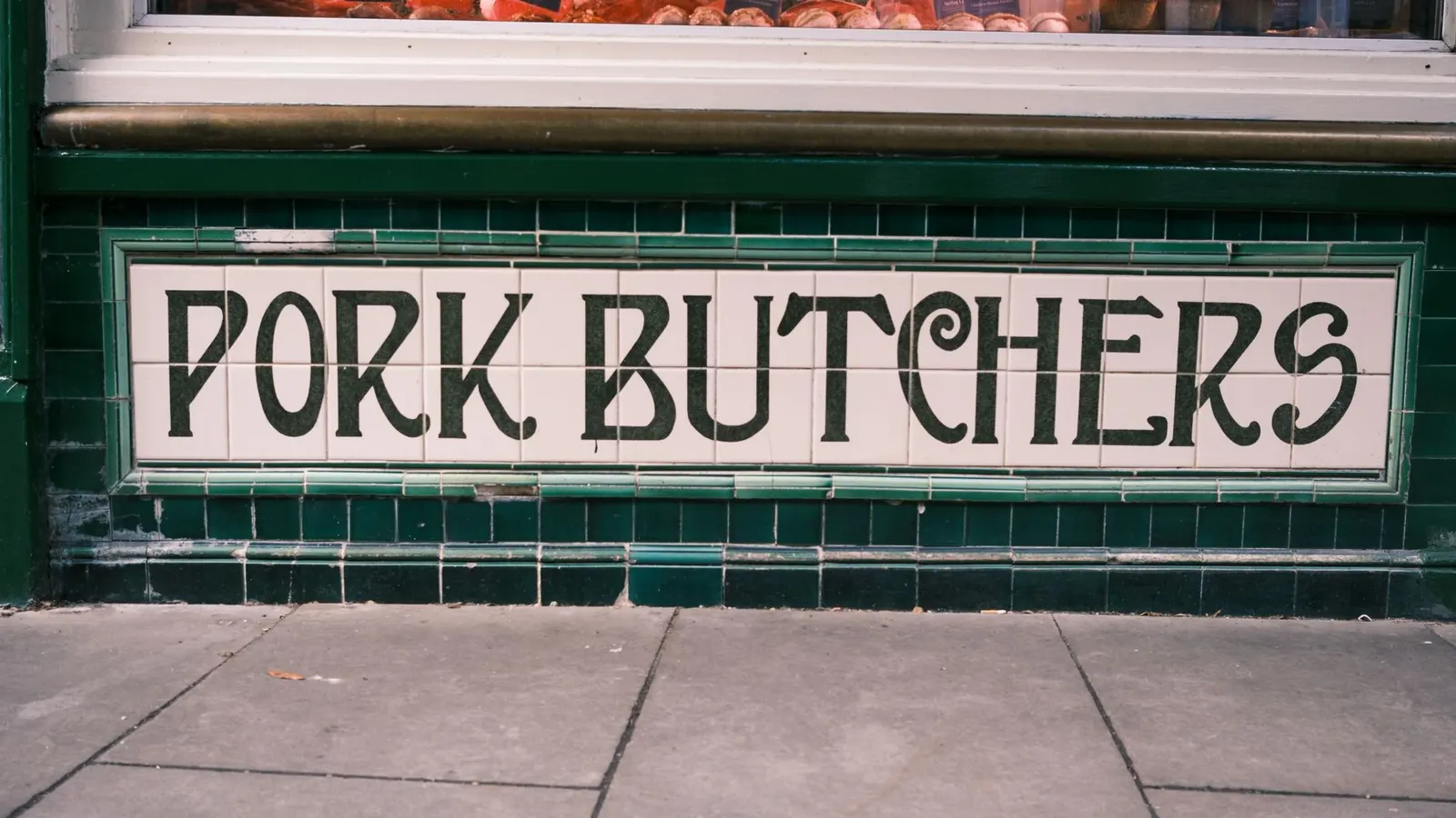 A hanging painted sign for a traditional pork butcher's shop on an English high street