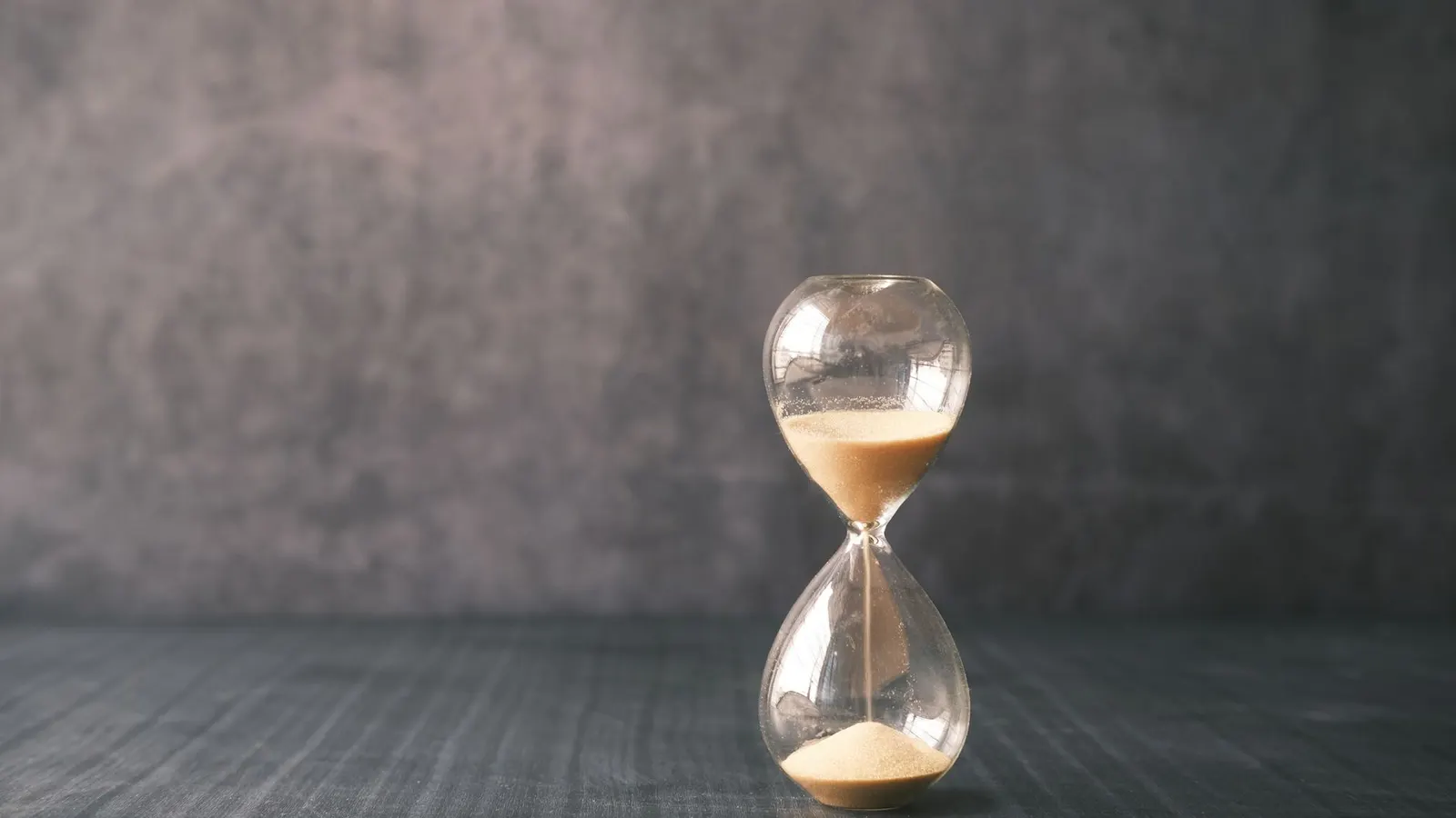 A glass hourglass photographed close up, the sand part run through into the lower bulb