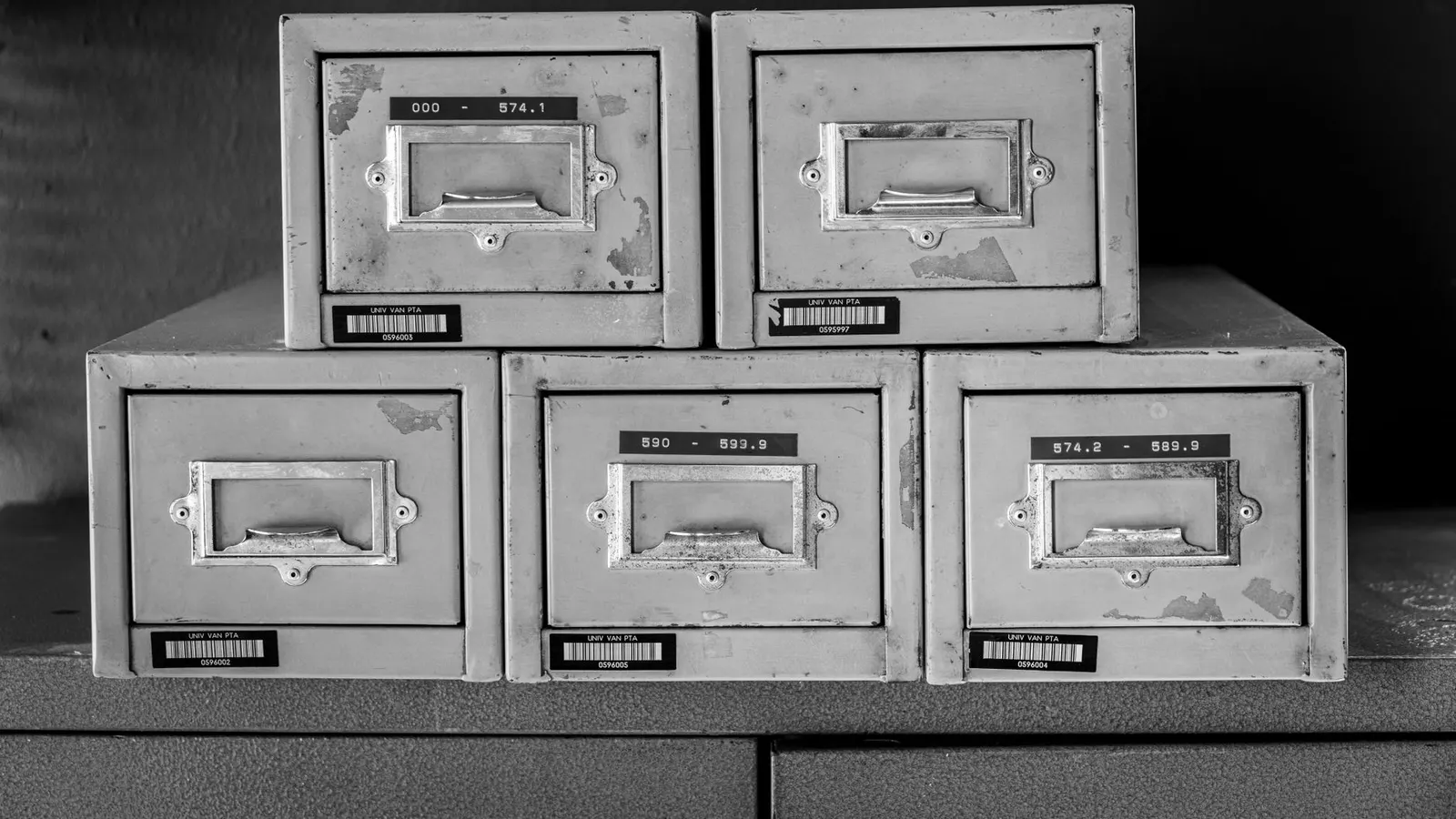Five worn metal filing cabinets standing in a row, drawers closed, photographed in black and white