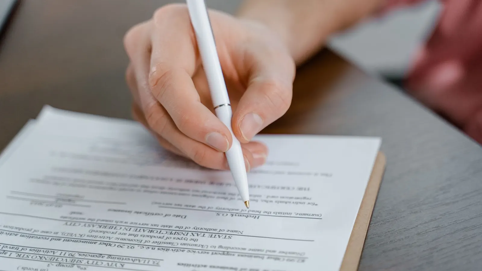 A hand signing the foot of a printed document with a ballpoint pen, the page held in sharp focus