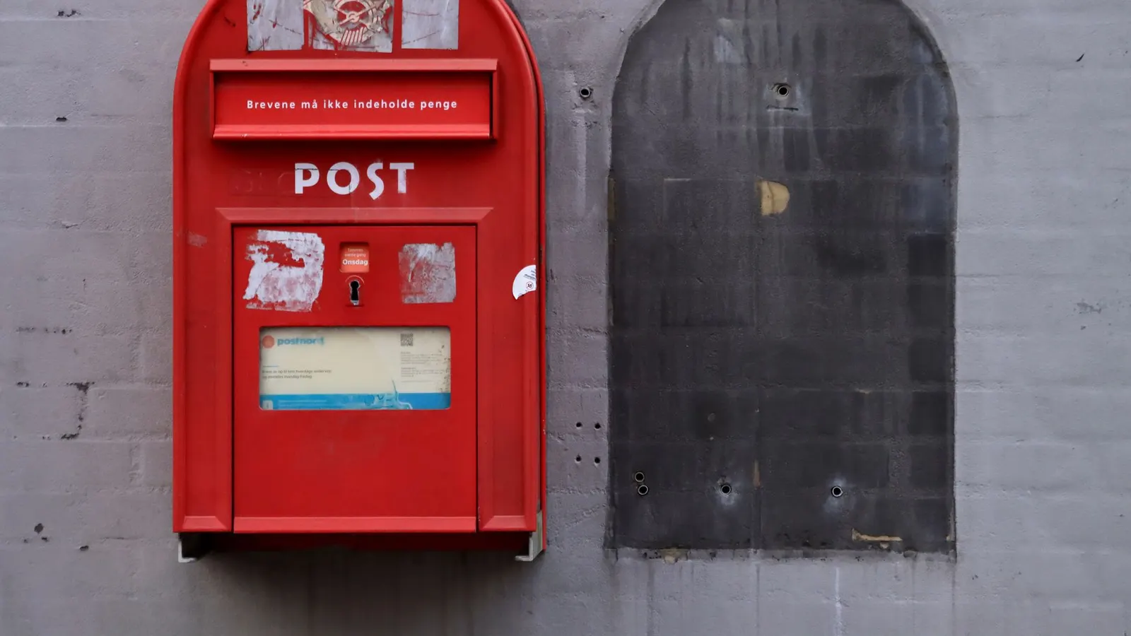 A red Royal Mail post box set into a grey urban wall